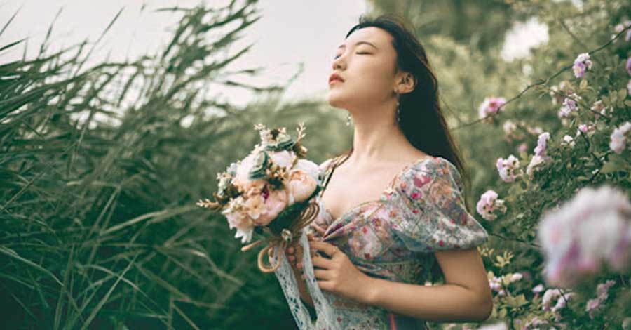 Asian woman holding a bouquet of flowers in a field.