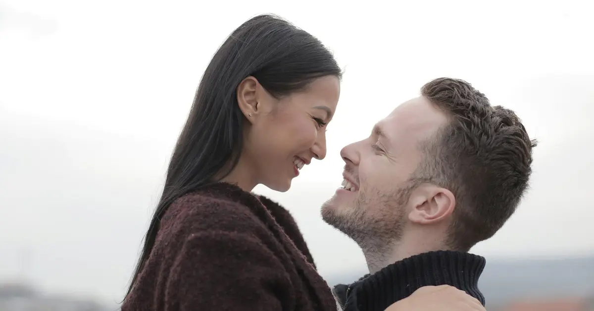 A photo of a western man and Asian woman hugging while happily looking at each other